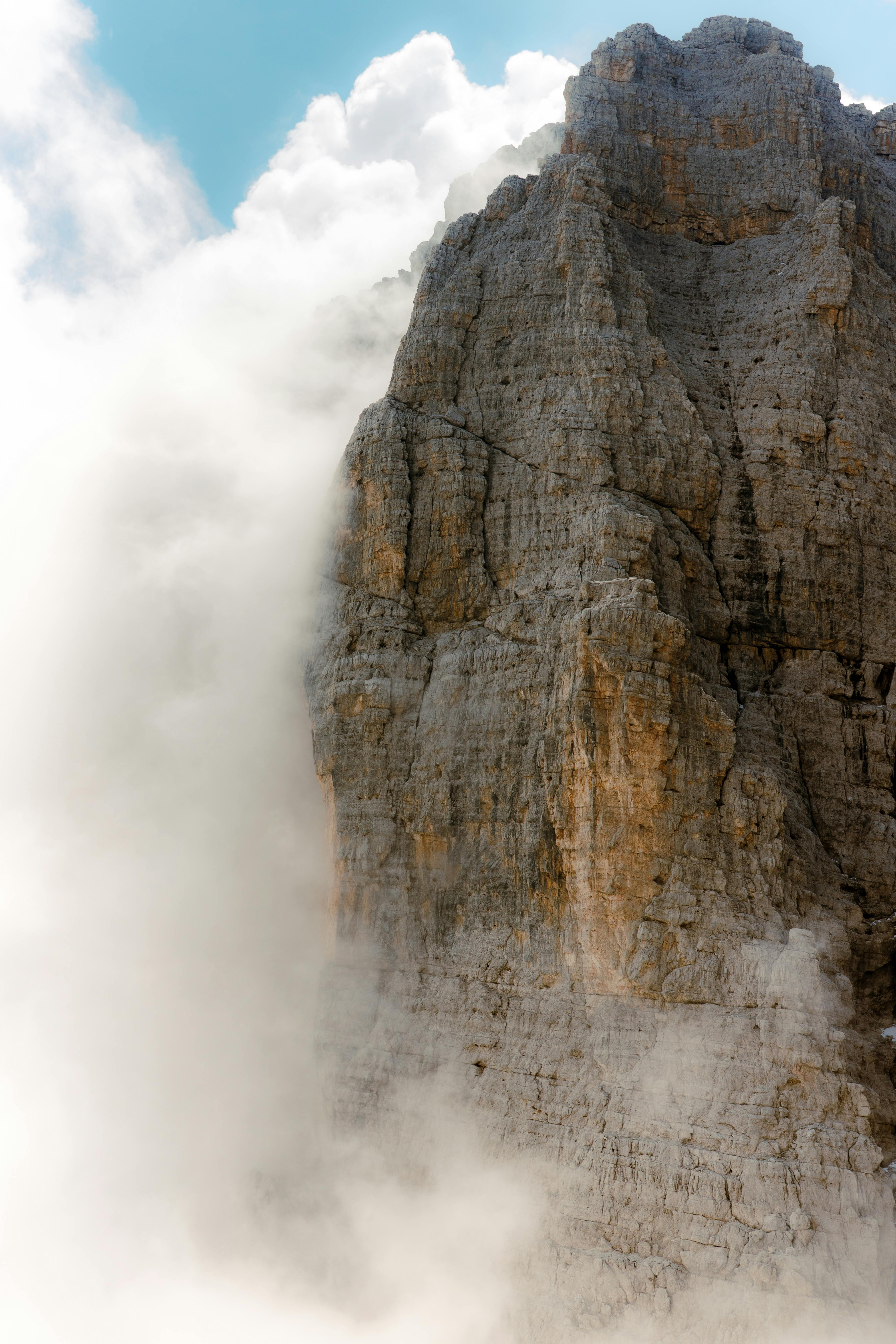 Dramatic view of a rugged mountain peak enveloped by misty clouds under a clear sky.