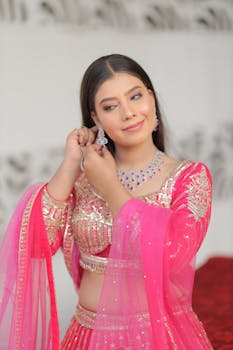 A beautiful Indian bride in a pink lehenga adjusts her earrings with elegance.