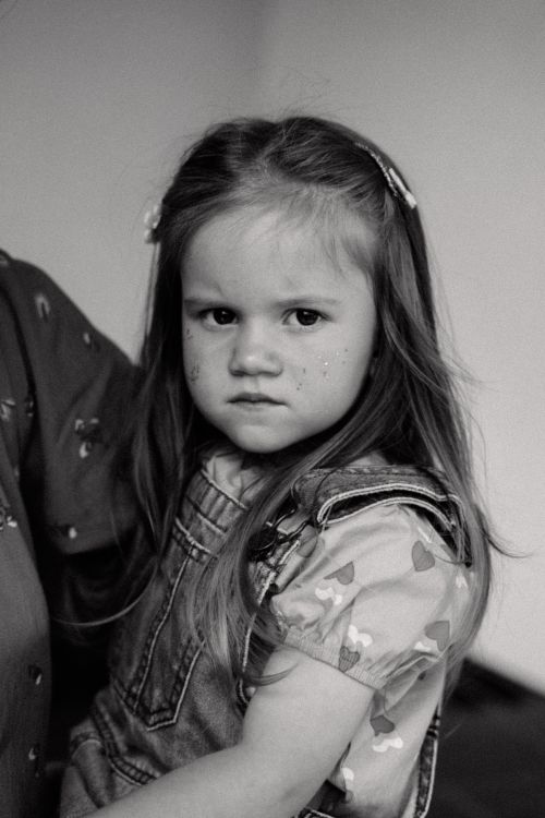 Free A thoughtful young girl in overalls with delicate face paint, captured in monochrome. Stock Photo