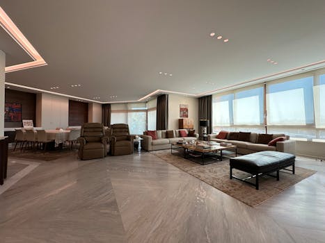 Elegant and spacious modern living room with panoramic windows, stylish furniture, and warm lighting, creating a cozy ambiance.