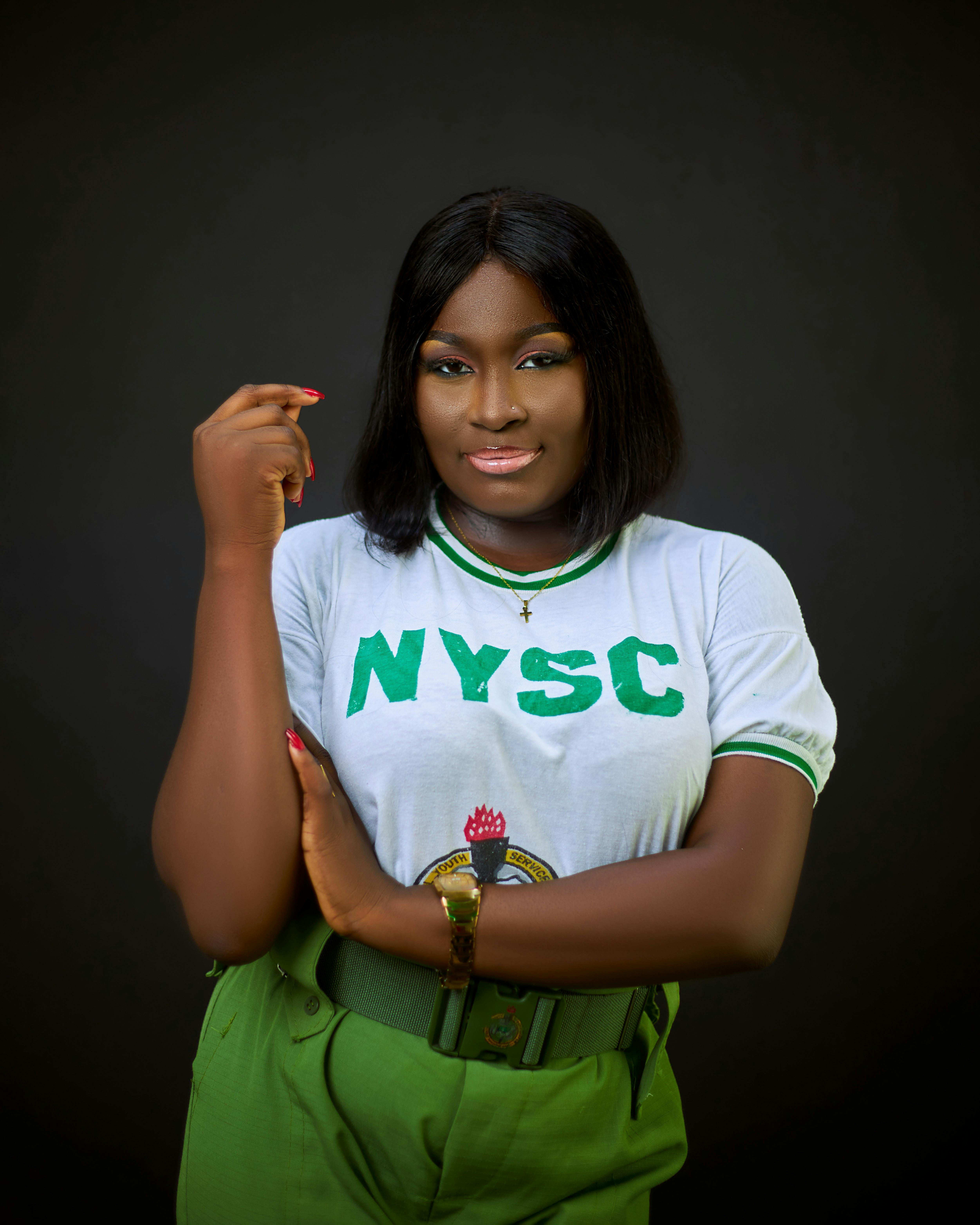 Portrait of a confident young African woman wearing an NYSC uniform, smiling against a dark background.