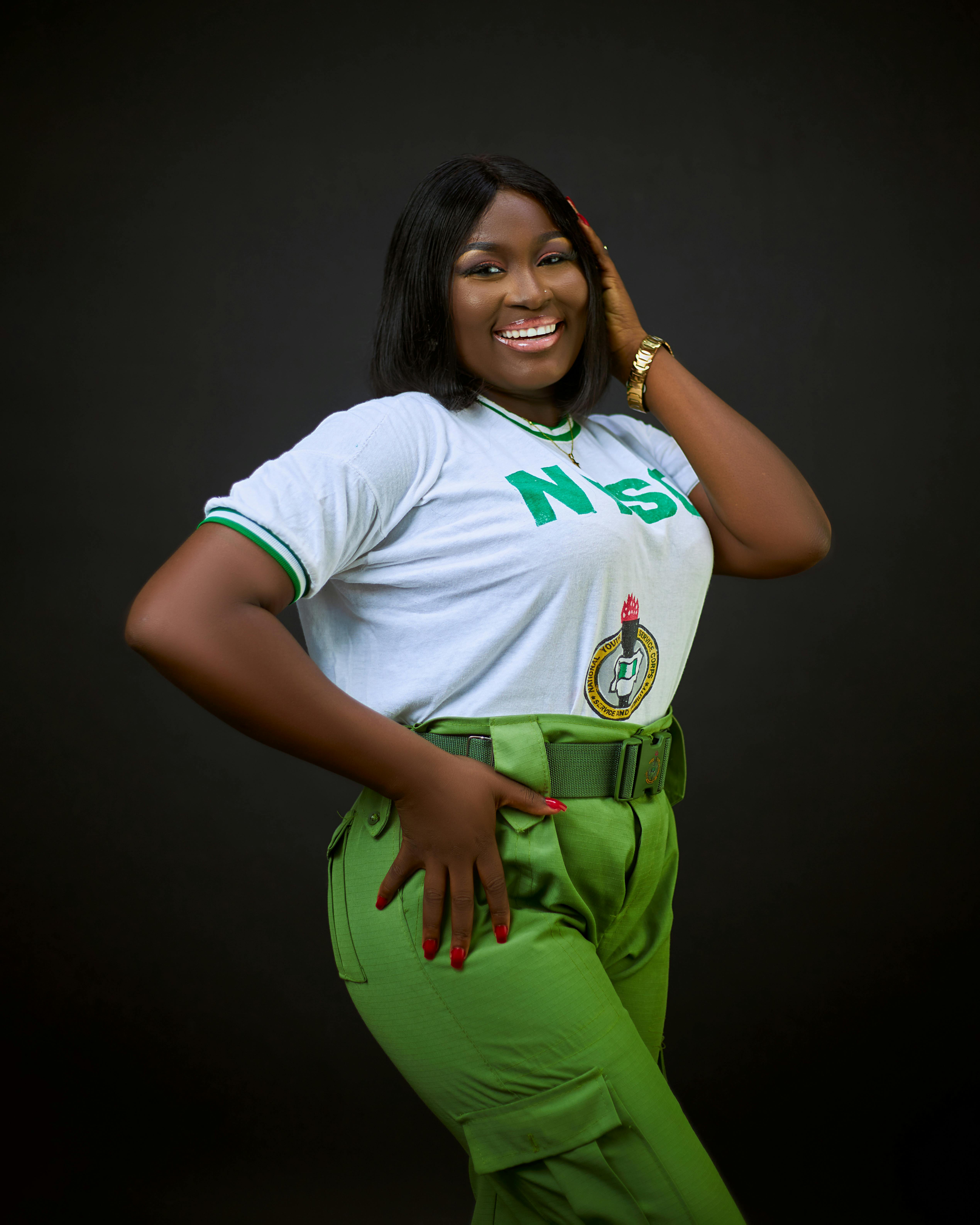 Joyful woman in NYSC attire posing confidently against a dark background.