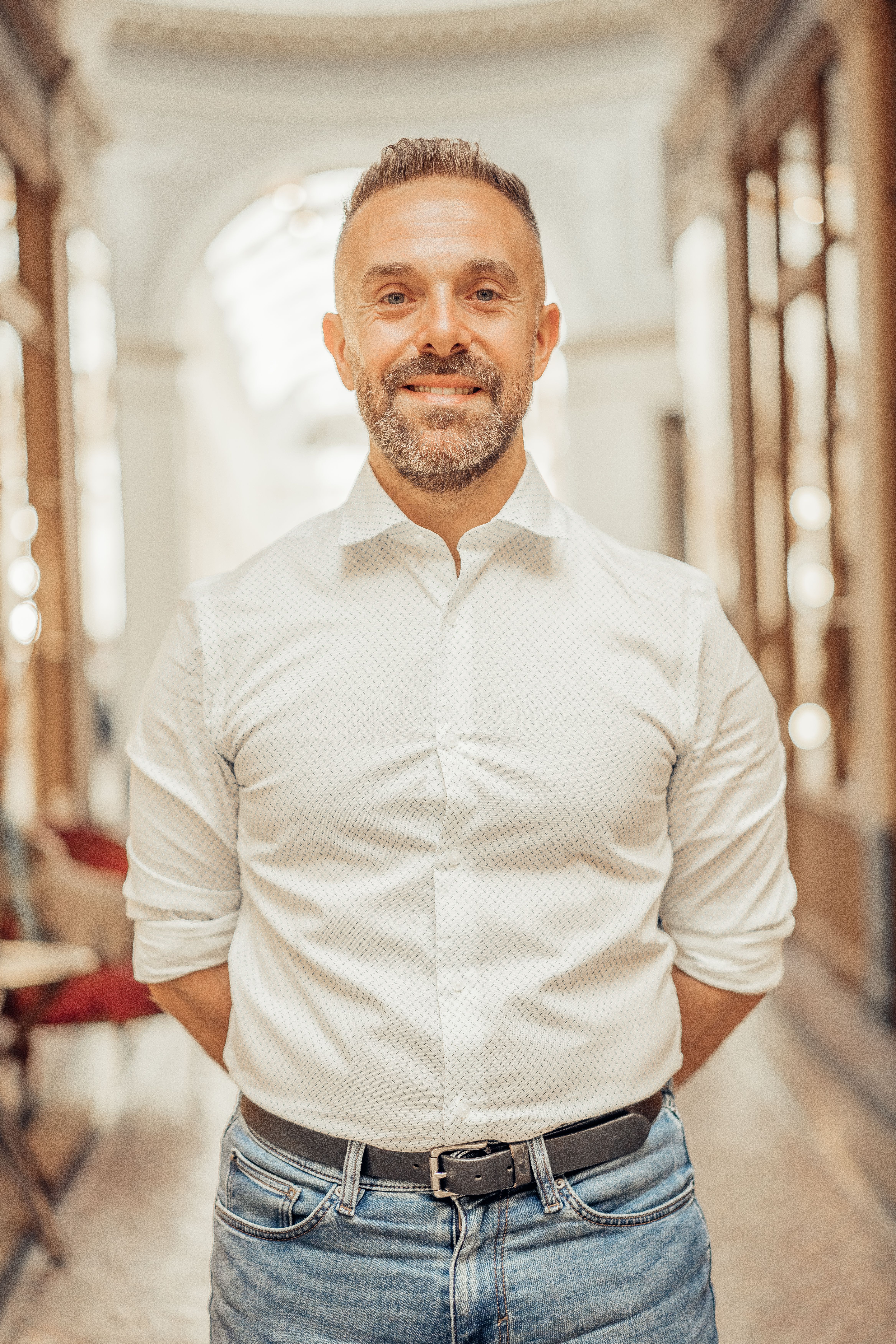 A cheerful adult man posing inside a classic Parisian arcade. Stylish, warm ambiance.