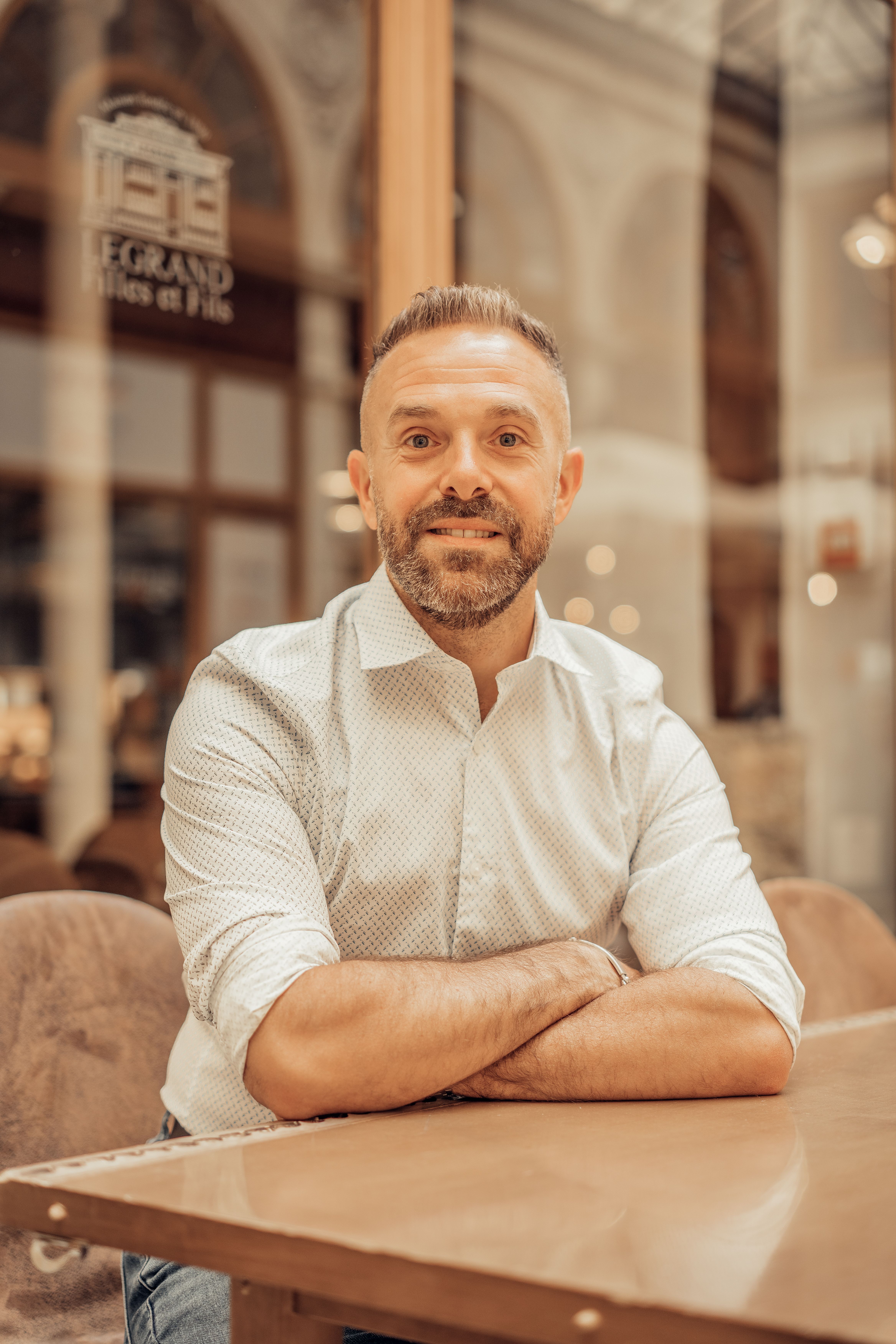 Smiling man sitting in a Parisian café, enjoying a relaxed moment indoors.