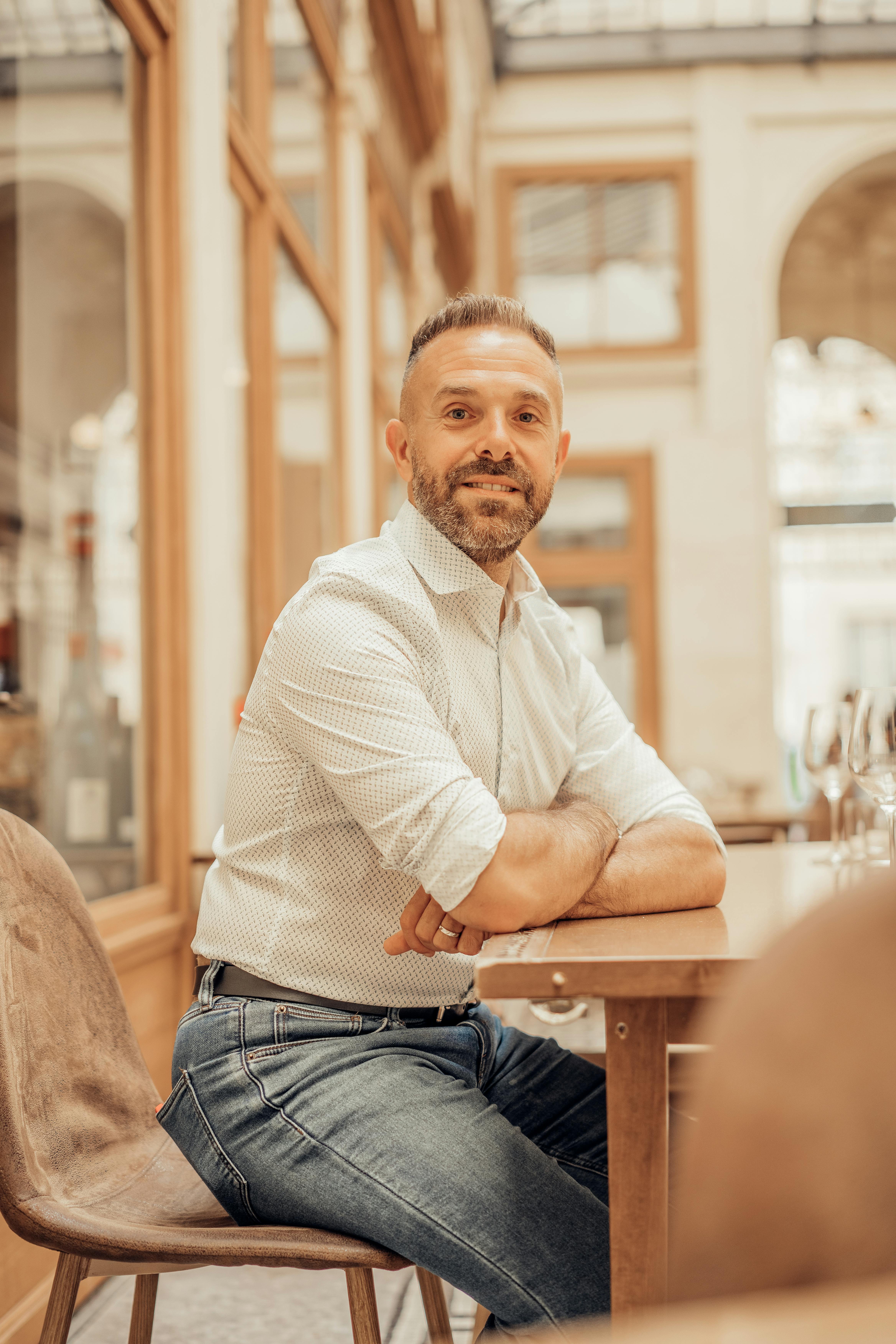 Man smiling and sitting in a chic Parisian café with modern decor.