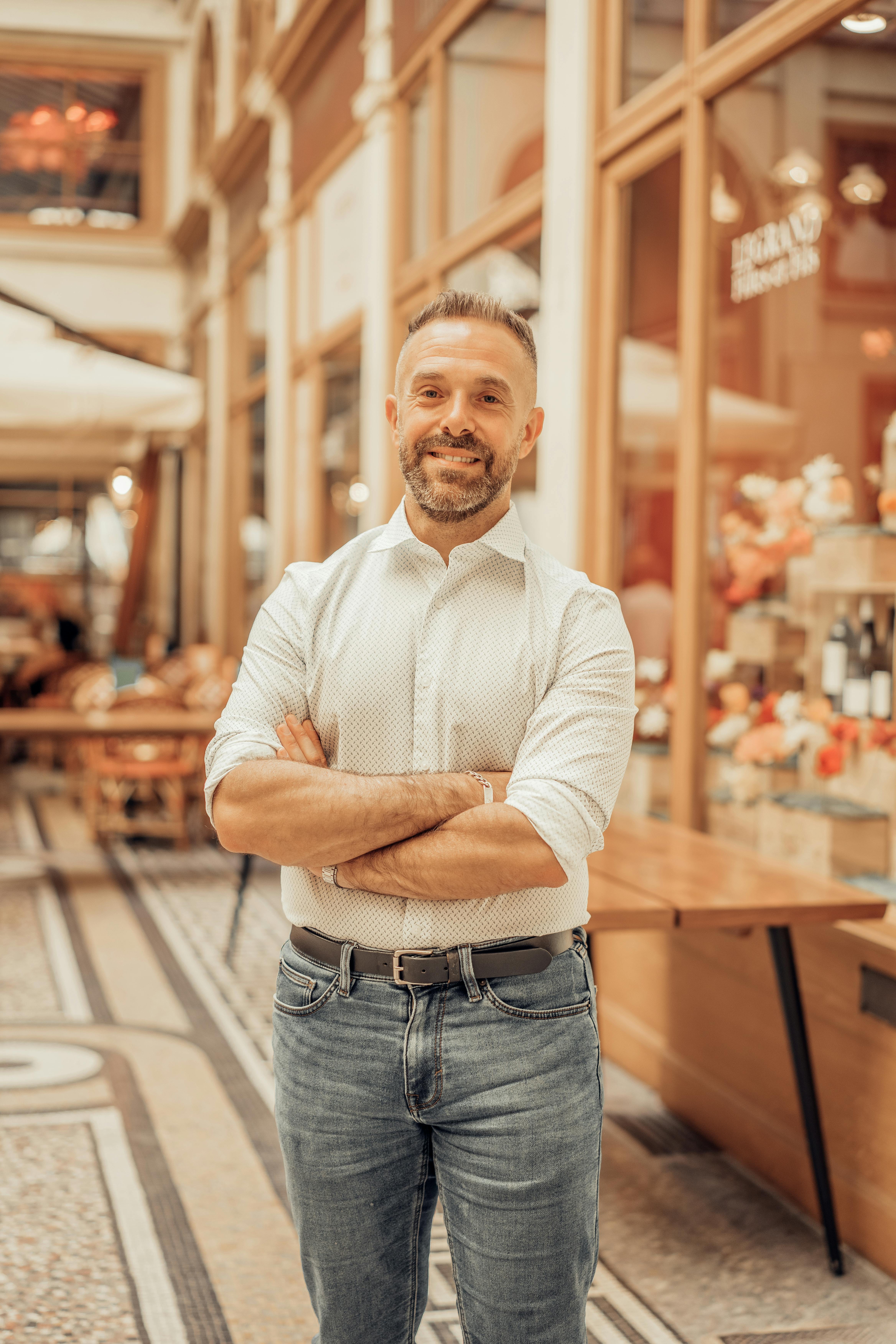 Confident man smiles while standing in a stylish Parisian passageway.