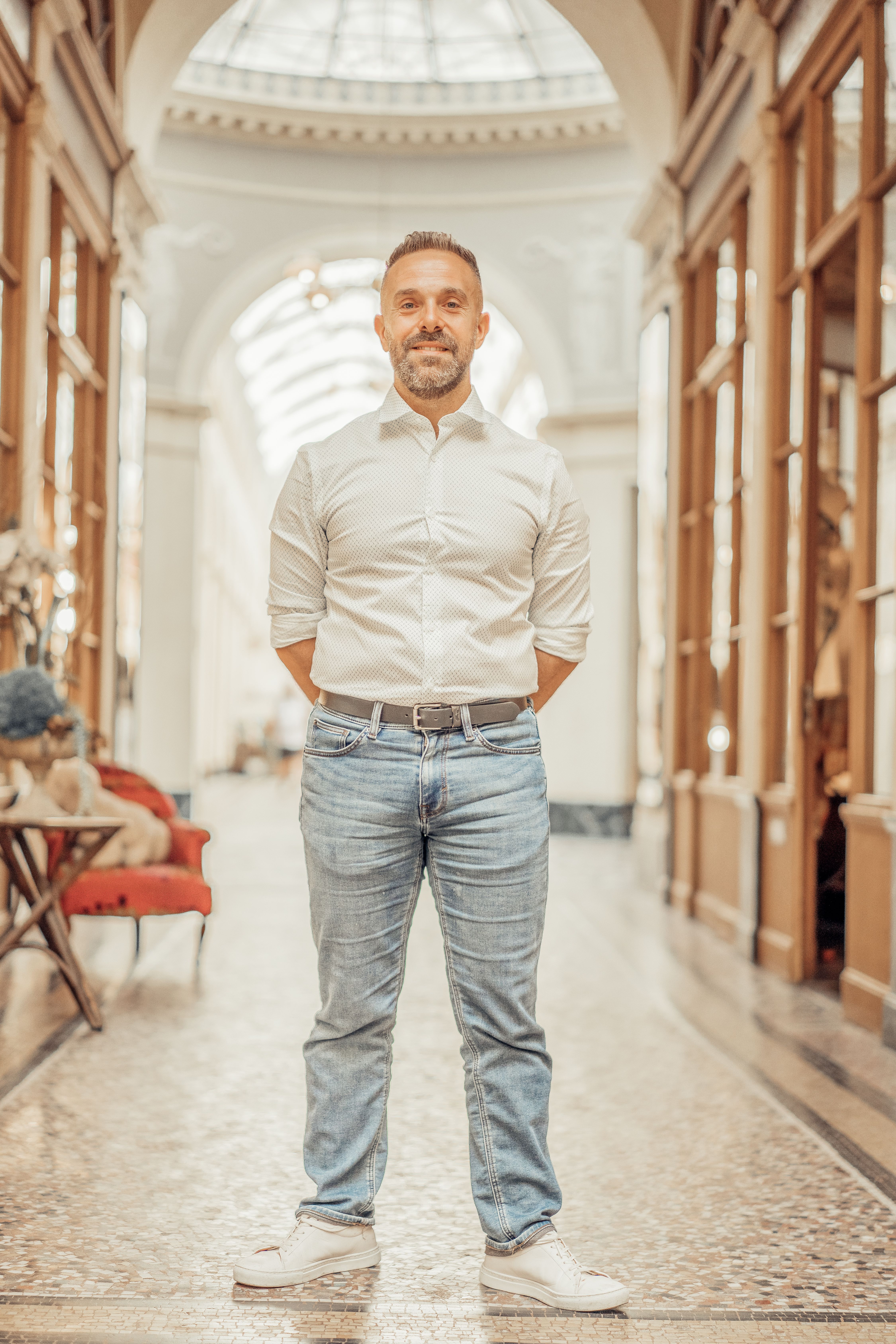 Caucasian man in casual attire standing in elegant Parisian passageway indoors.