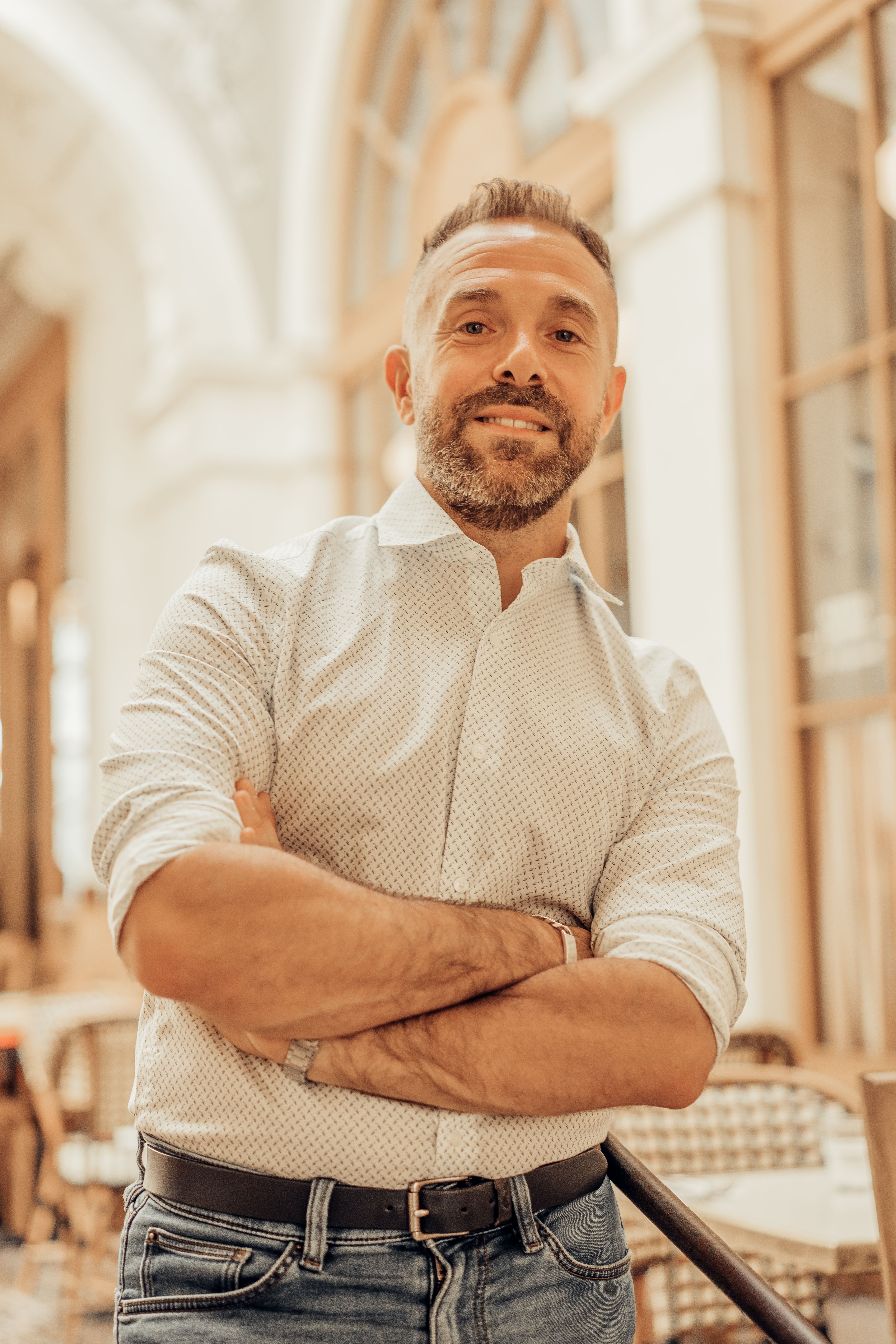 A man stands confidently indoors, exuding sophistication in a Parisian café environment.
