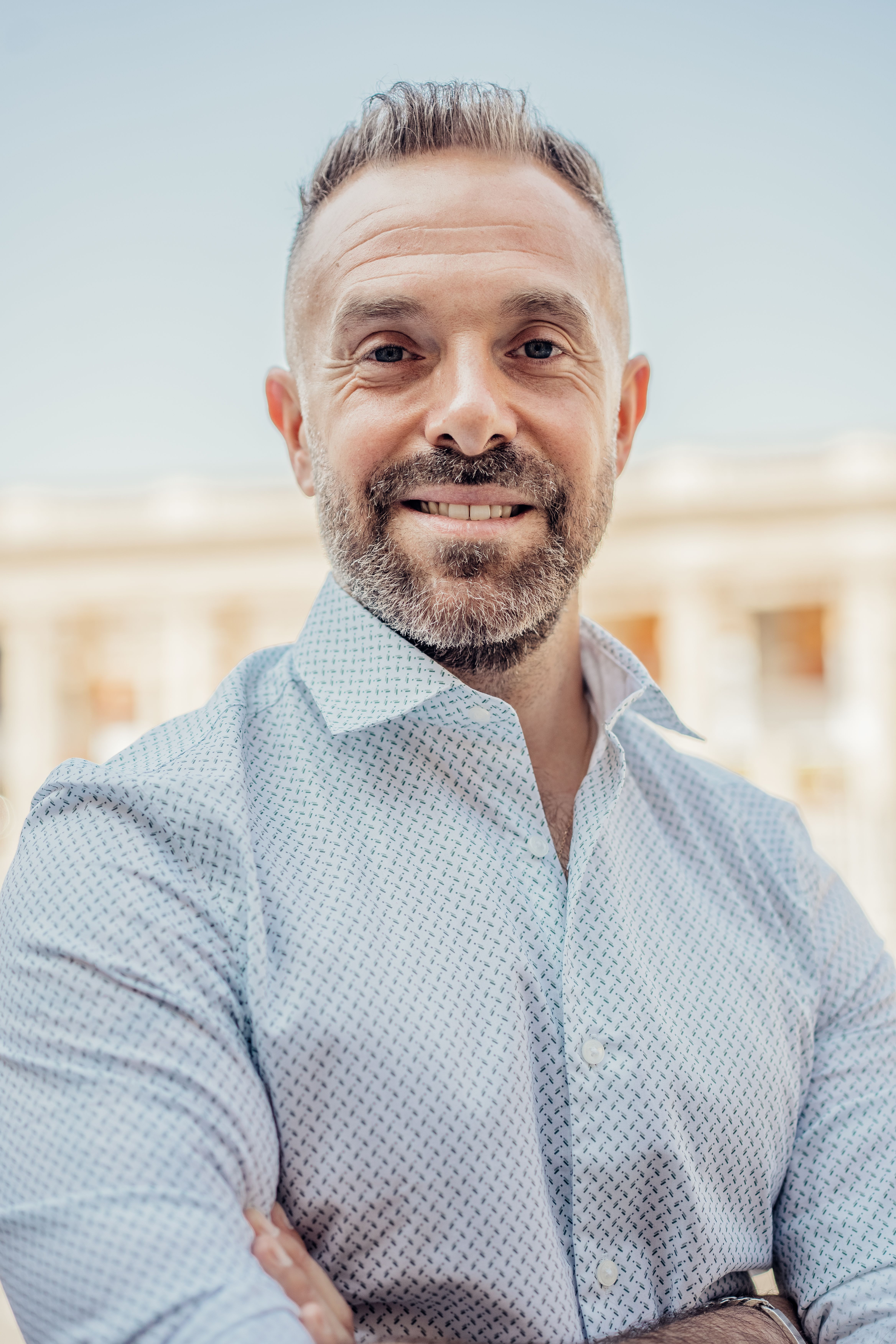 Portrait of a confident man smiling with a Parisian backdrop. Captured outdoors with a bright, warm tone.