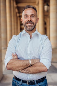 Confident man standing with crossed arms in a historic Parisian arcade, exuding professionalism and style.
