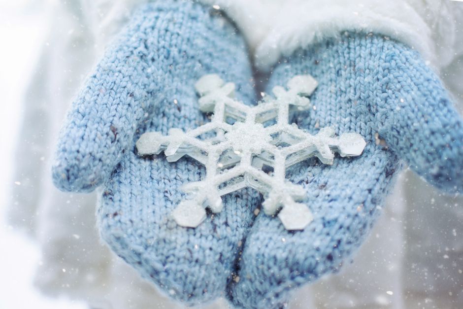 Close-up of hands in blue gloves holding a snowflake during a snowy winter day.