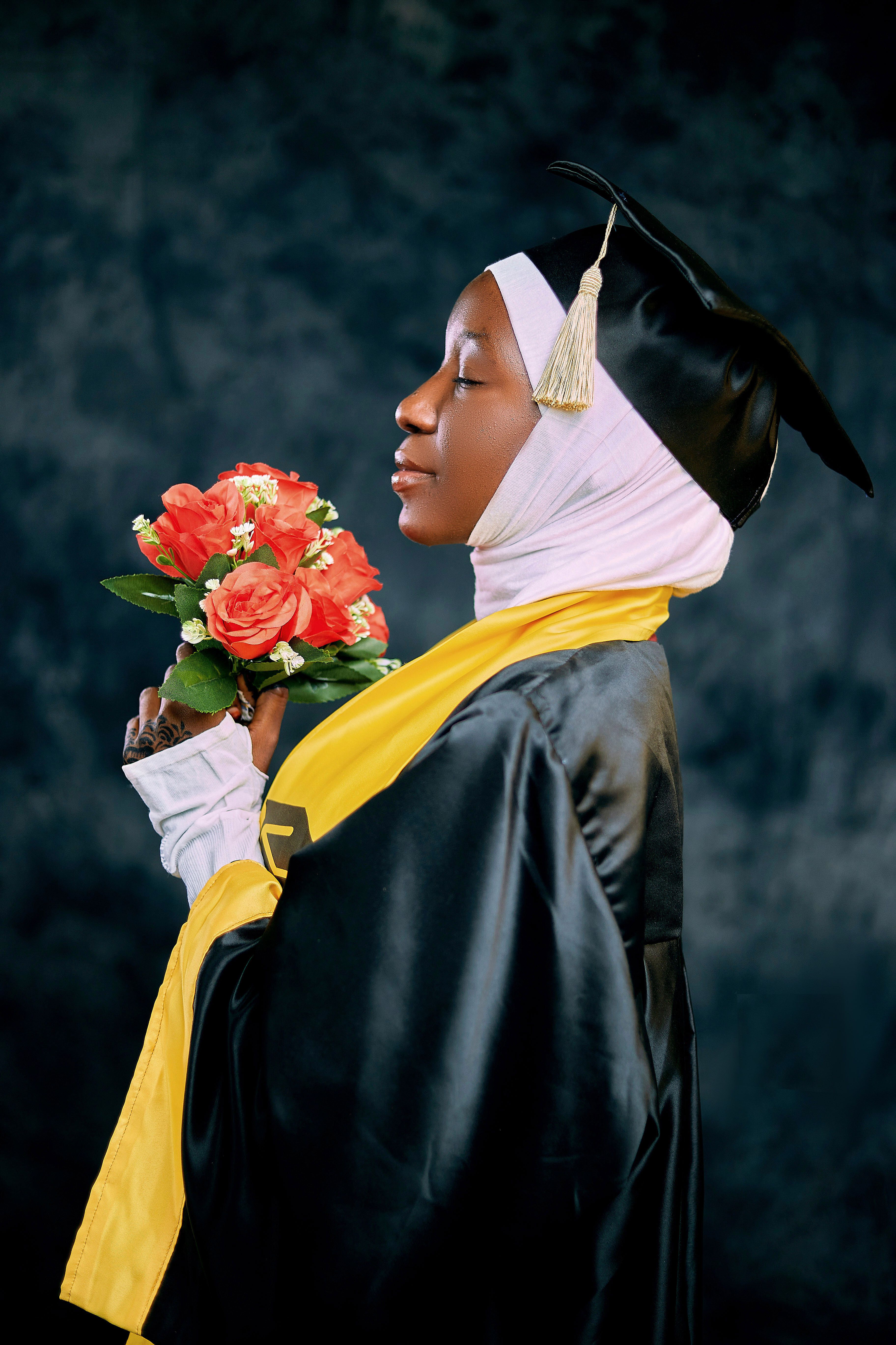 Profile of a young female graduate wearing hijab and cap, holding flowers.