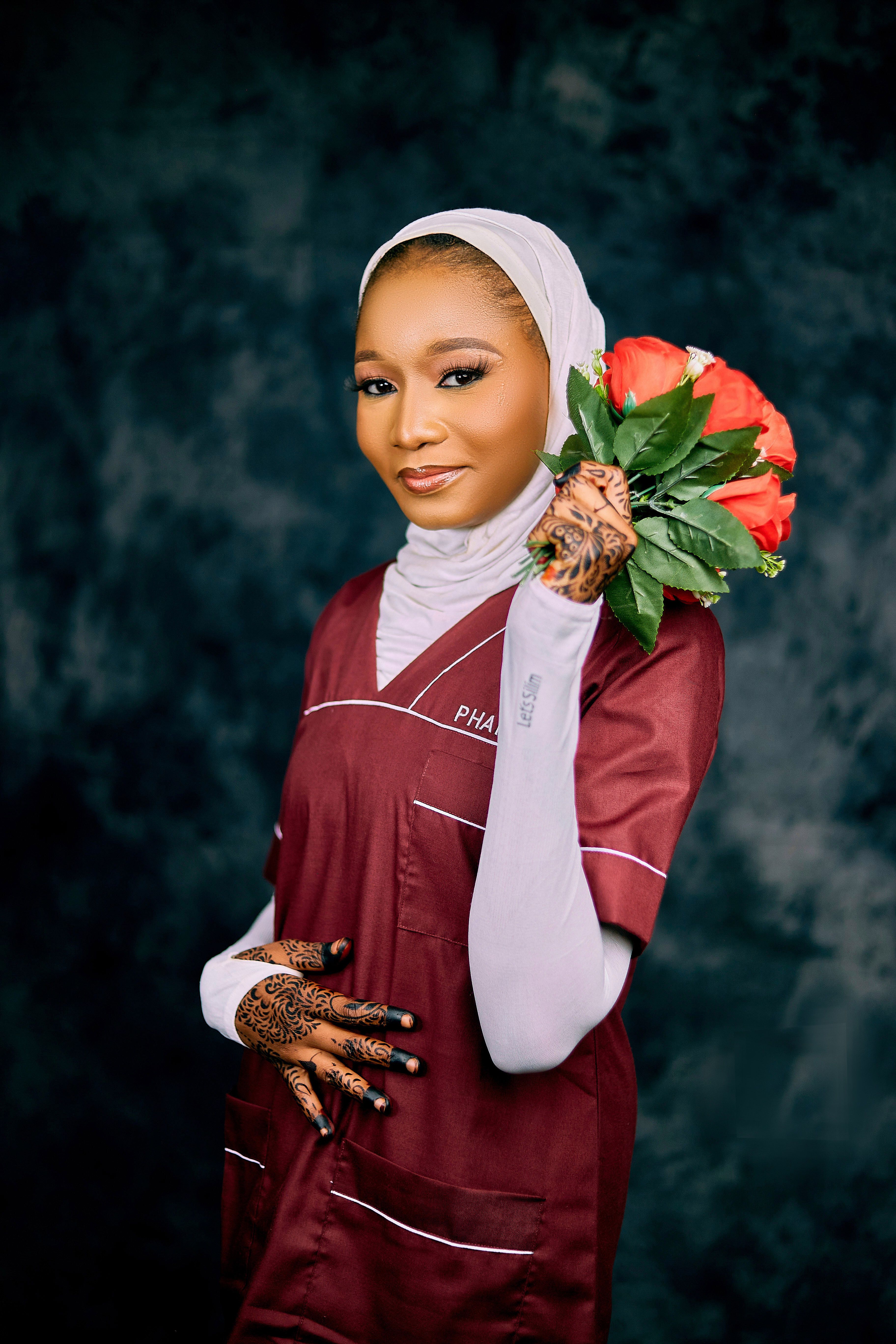 Elegant portrait of a woman in a maroon outfit holding a bouquet with henna-adorned hands.