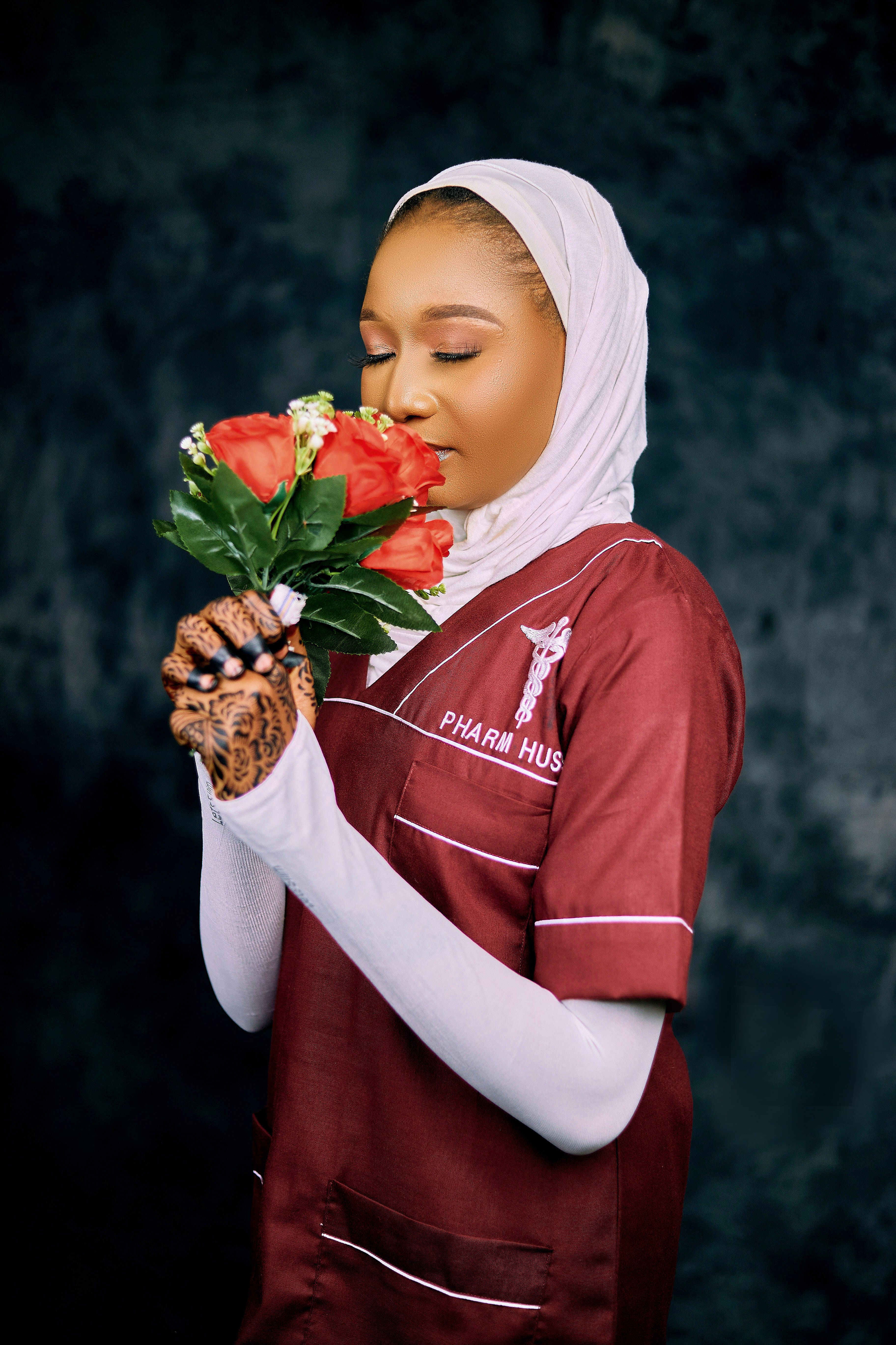 Nurse in uniform with henna hands holding red roses against a dark background.