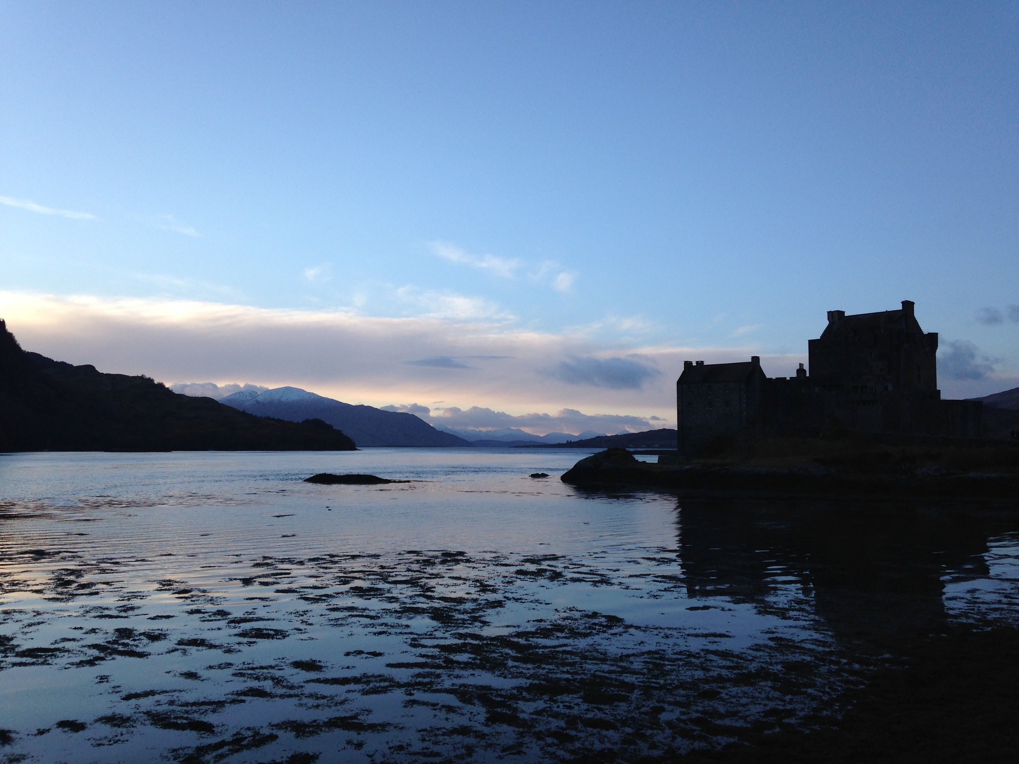Eilean Donan Castle silhouetted against a tranquil twilight sky in Scotland, reflecting on calm waters.