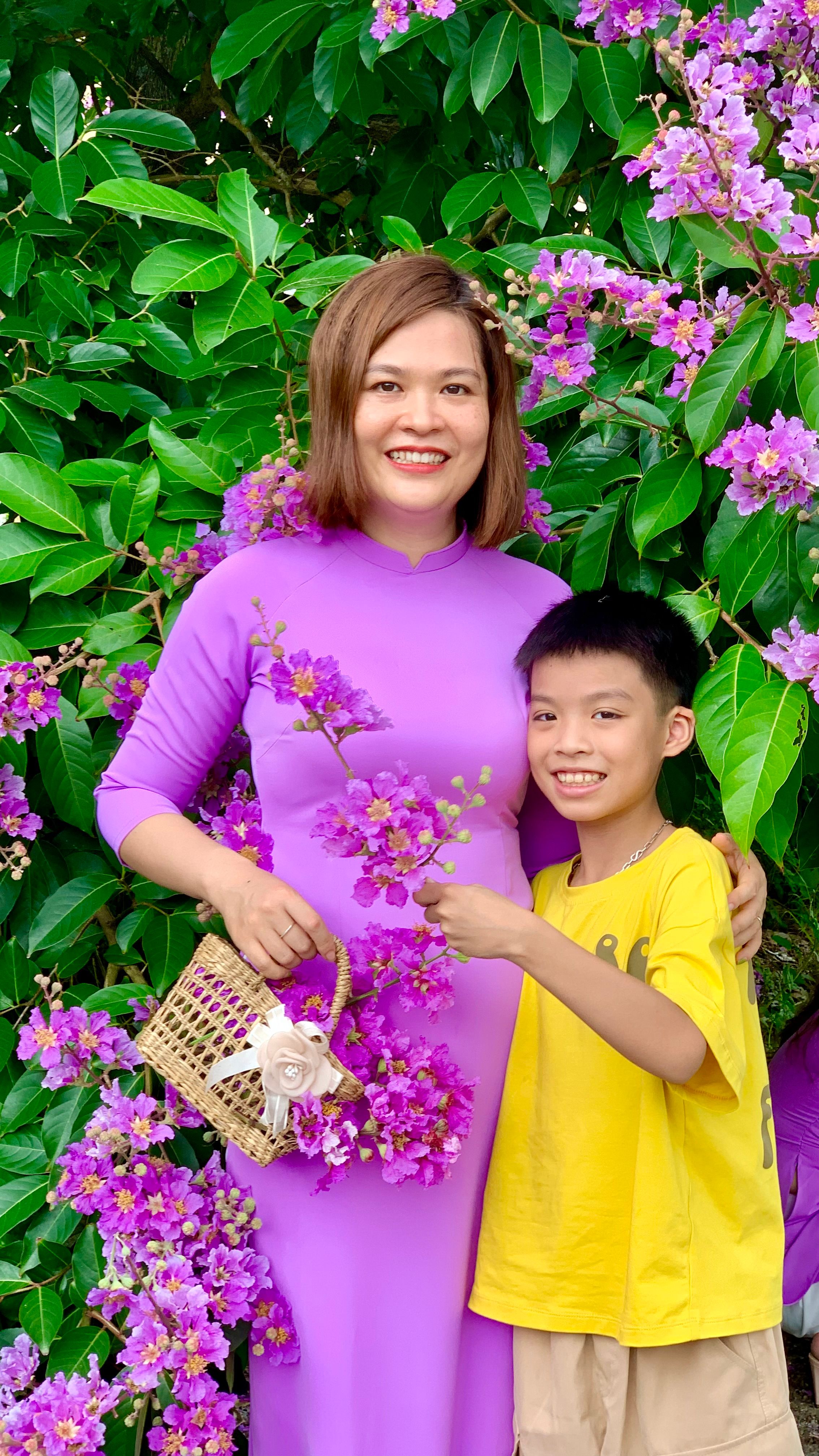 Mother and son pose joyfully amidst vibrant purple flowers in Nam Định, Vietnam.
