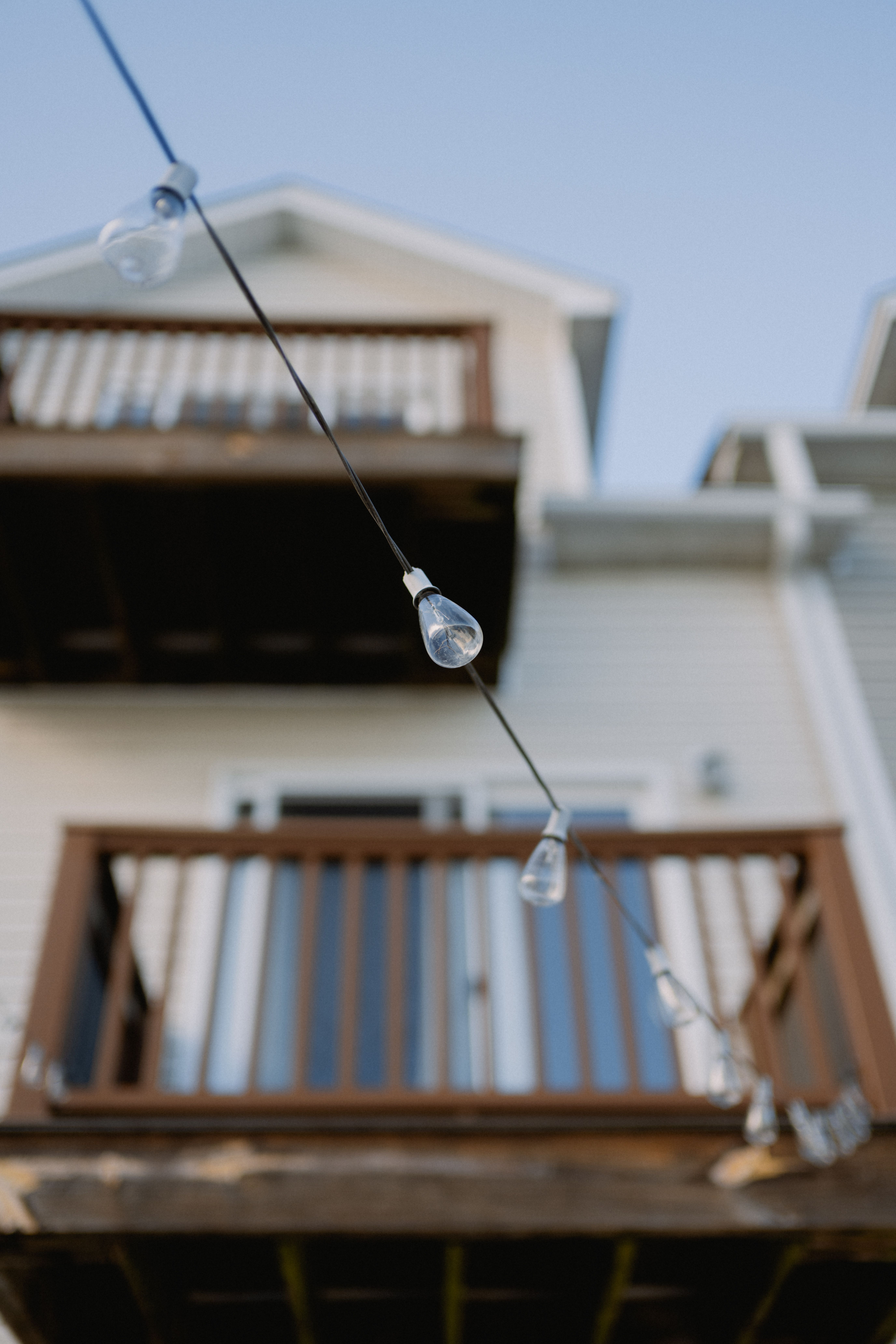 String lights clipped to the metal railing of a small apartment patio, glowing at dusk