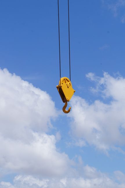 Yellow crane hook suspended in blue sky with clouds. Captured outdoors in Pará, Brazil.