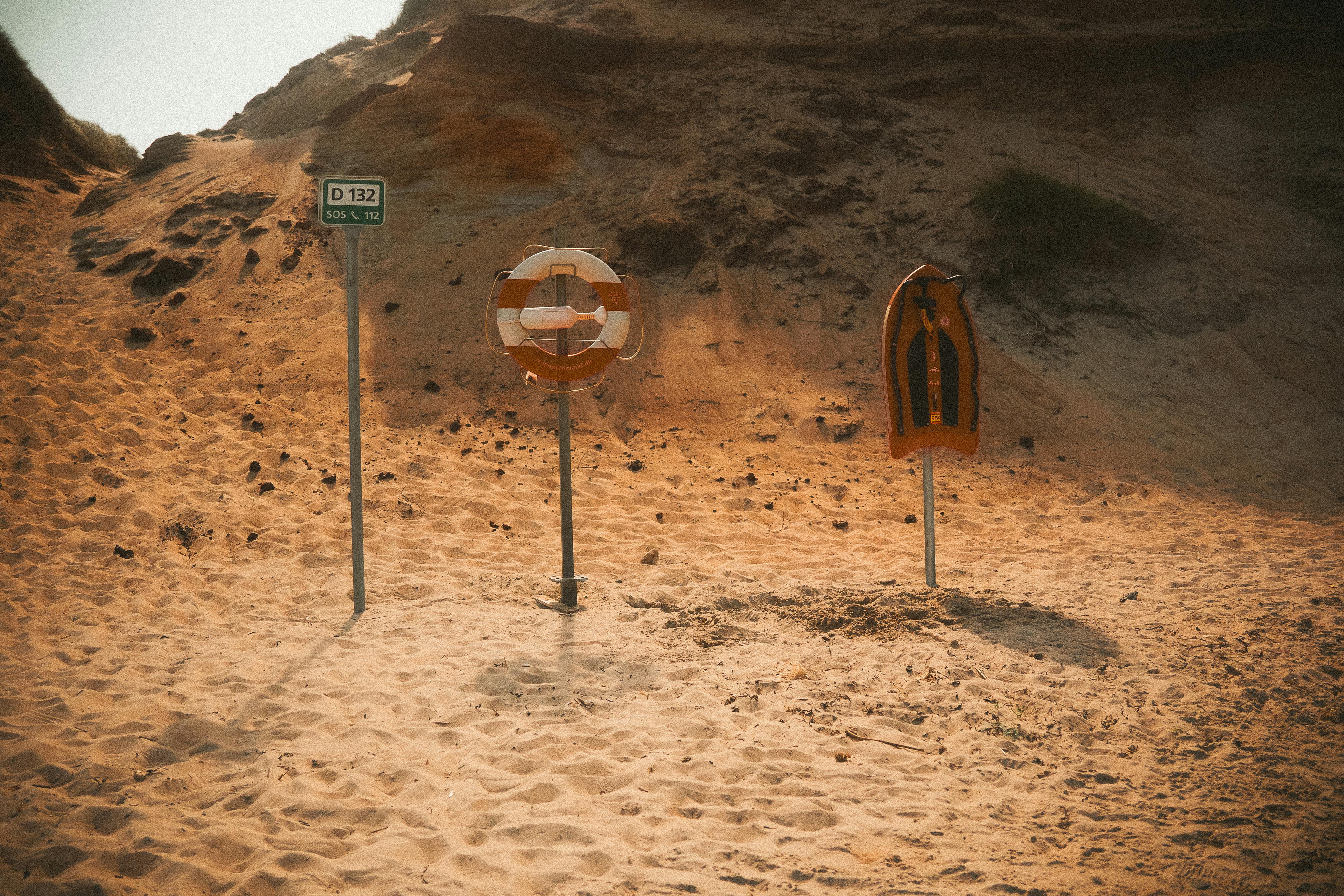 무료 따뜻한 햇살 아래 모래 언덕이 있는 모래사장에서 구조 링과 보드를 착용하세요. 스톡 사진