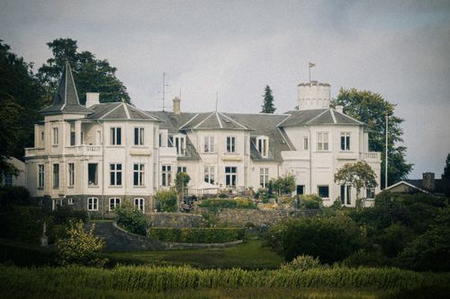 Free A classic European mansion surrounded by lush gardens, captured on a clear day with vintage charm. Stock Photo