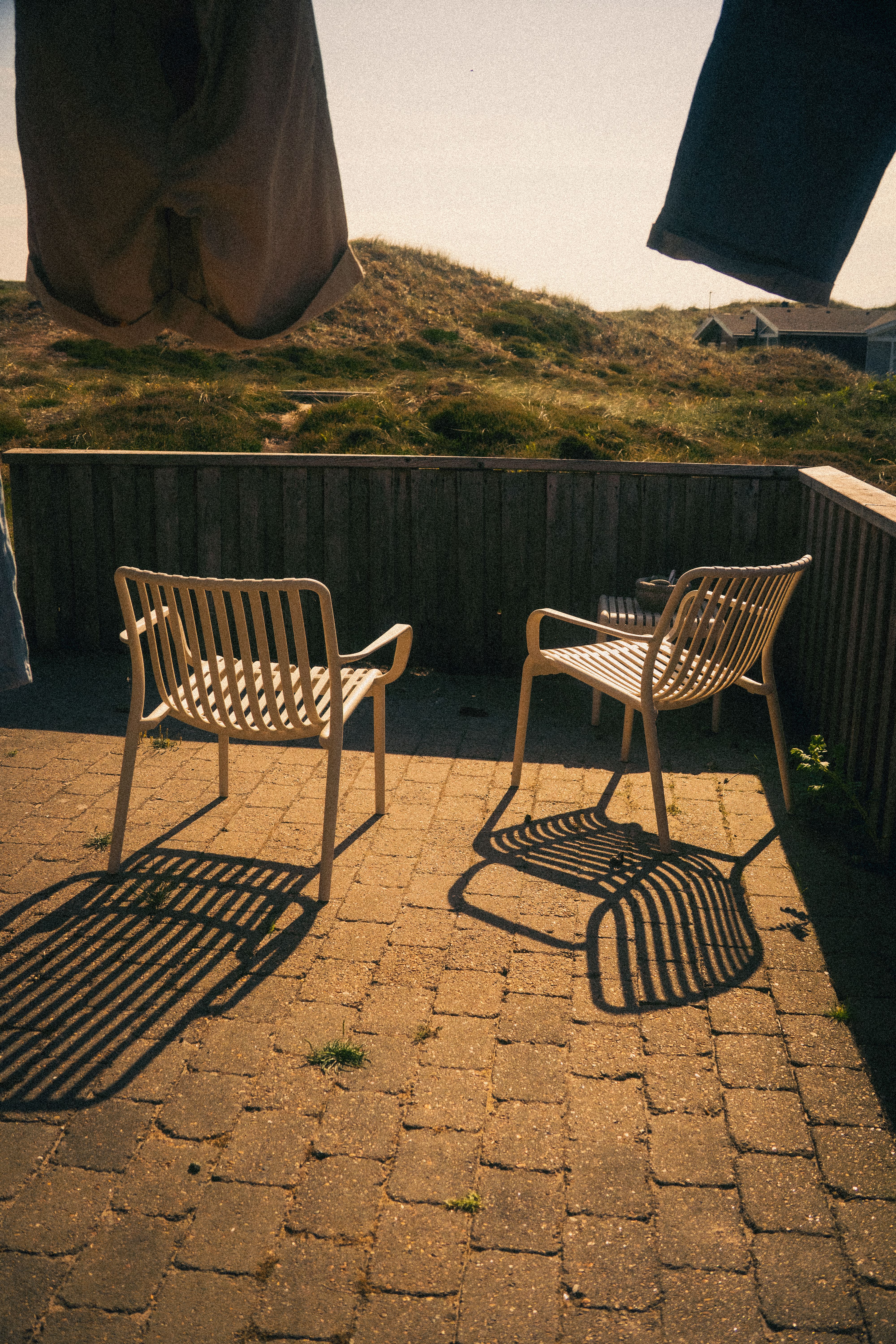 Two empty chairs with shadows on a sunny patio, offering a tranquil outdoor setting.