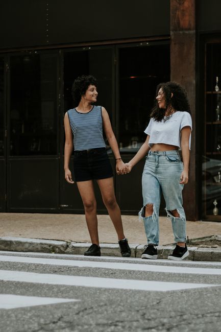 Two women joyfully holding hands on an urban pedestrian crossing, showcasing friendship.