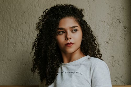 Free Elegant portrait of a woman with curly hair, red lips, and neutral expression indoors. Stock Photo