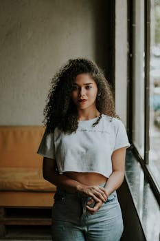 一位自信的女人卷发披肩，身着露脐上衣，在室内摆出姿势，尽显时尚风格