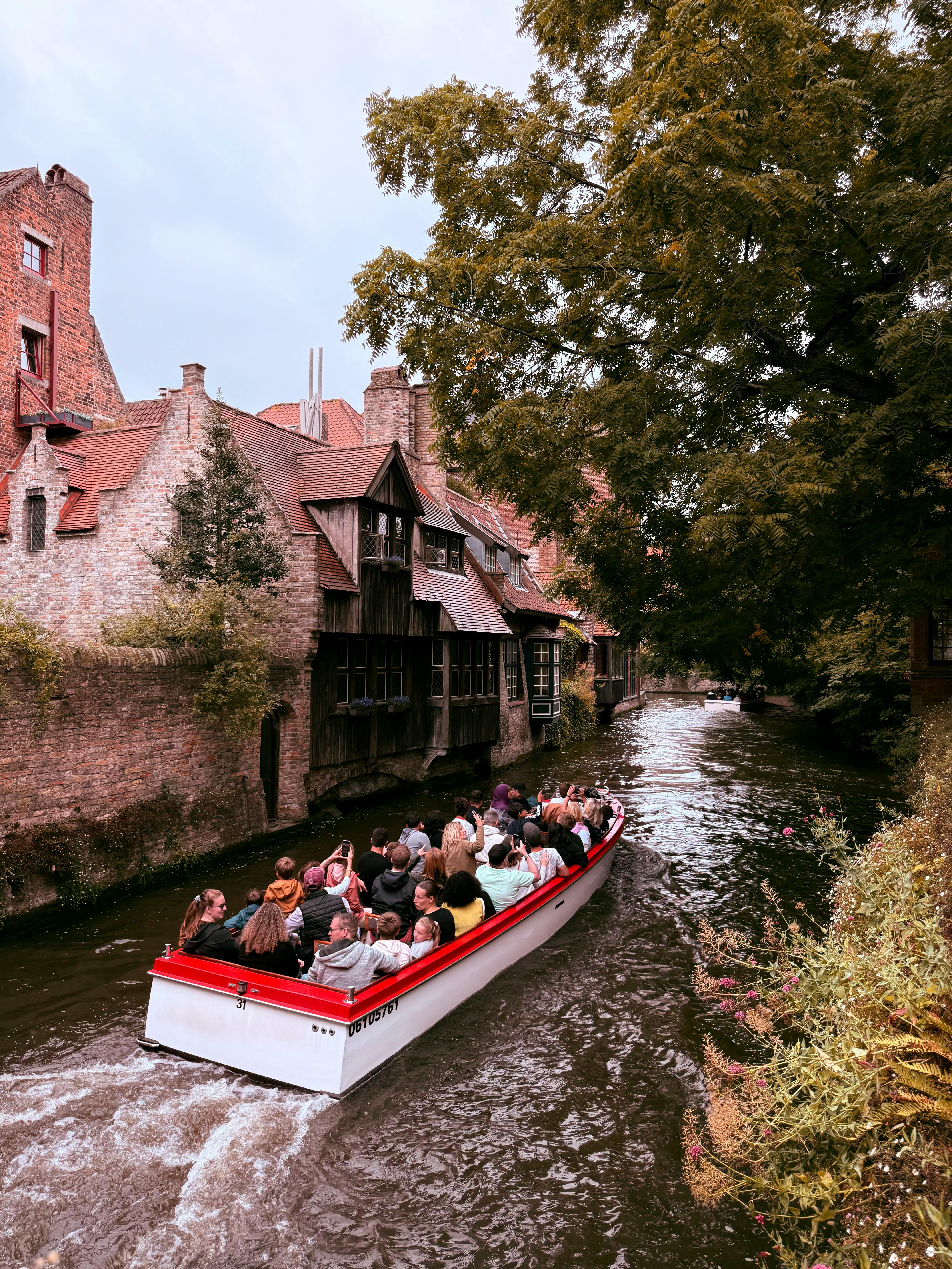 Picturesque canal in Bruges with tourists on a boat tour passing medieval buildings.