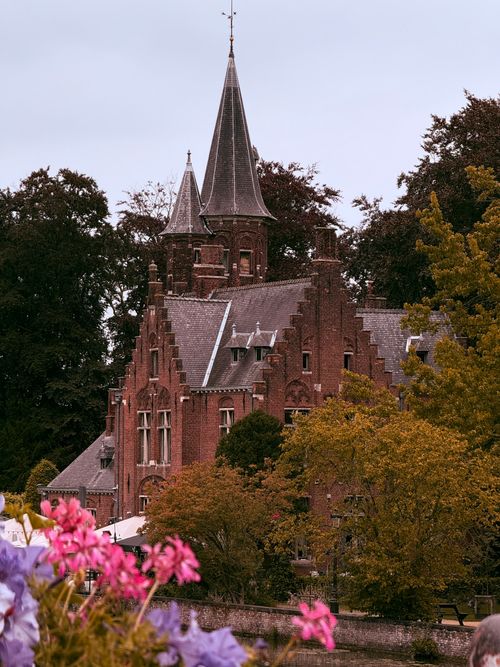 Free Stunning medieval castle in Bruges surrounded by autumn foliage and vibrant flowers. Stock Photo