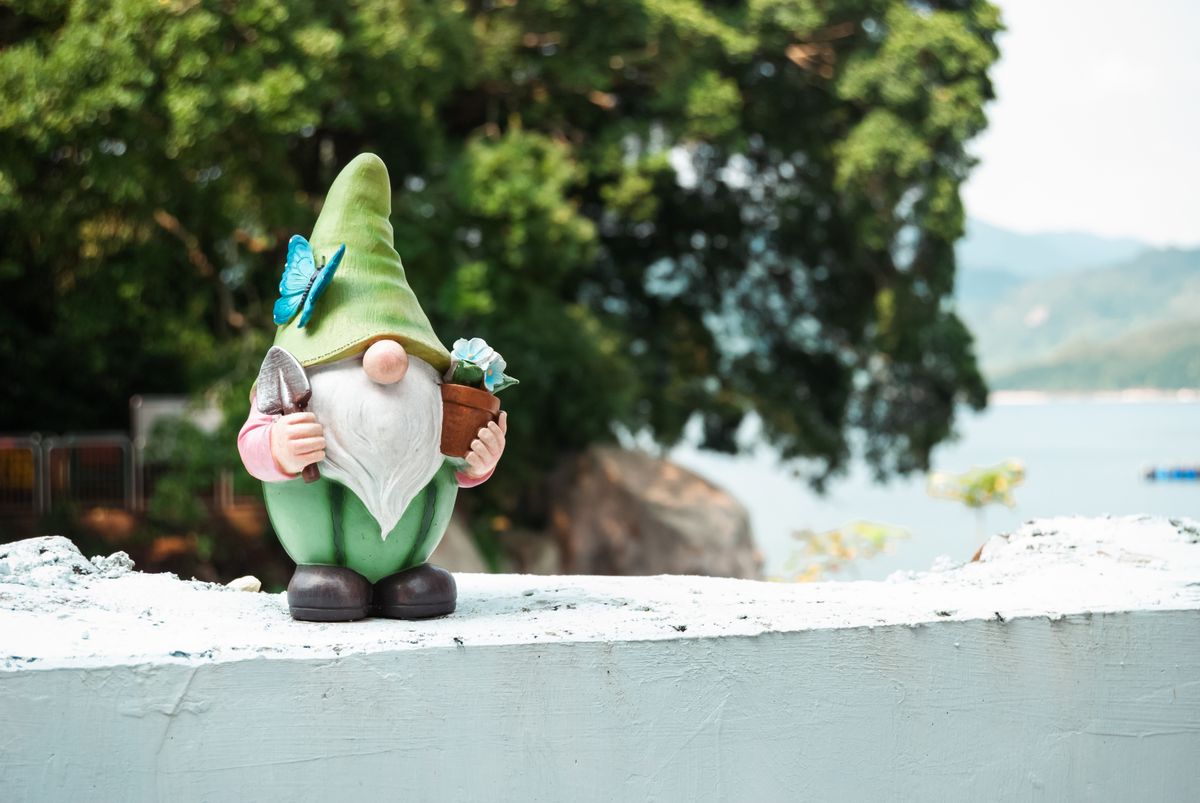 A charming garden gnome holding a pot and trowel, adorned with a butterfly outdoors. Stock Photo.