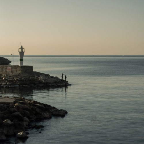 Free Calm seaside scene featuring lighthouse and fishermen at dusk. Stock Photo