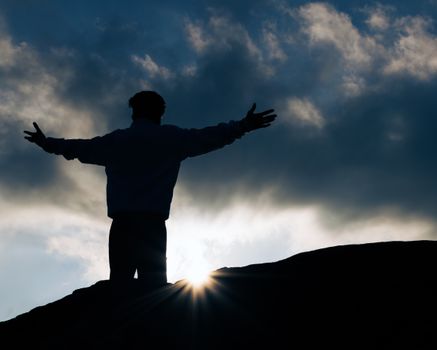 Silhouette view of a person with open arms at sunrise, symbolizing freedom and peace.