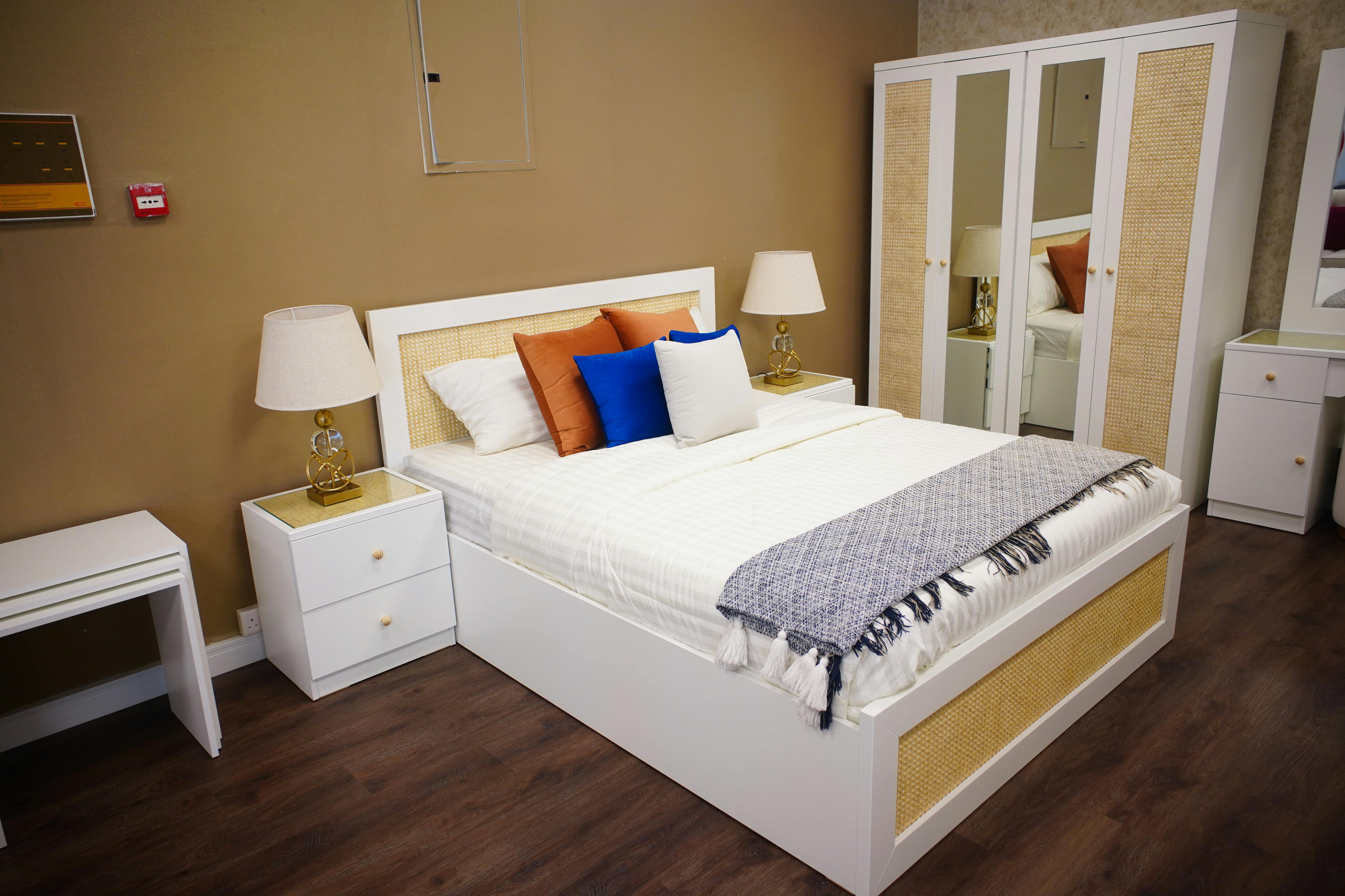 White bedroom set with bed, nightstands, and wardrobe, featuring gold accents, lamps, and pillows.