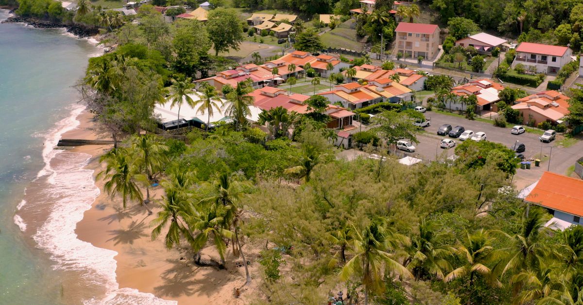 Aerial view of a tropical beachfront community with lush greenery and vibrant rooftops.