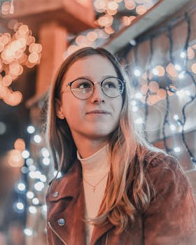 一幅戴着眼镜、面带微笑的女性肖像，周围环绕着散景和节日灯光，营造出温暖的氛围