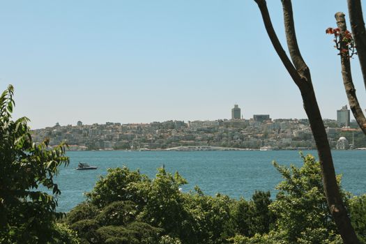 Beautiful view of Istanbul cityscape across the Bosphorus Strait with lush greenery and a passing boat.