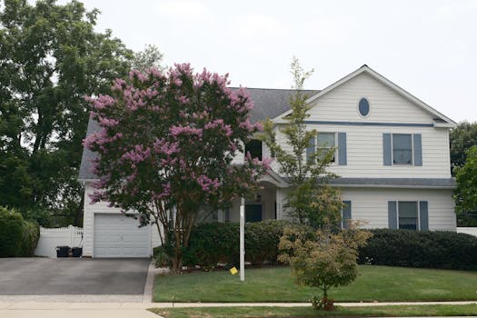 Front view of a suburban house with a blooming crape myrtle tree in the garden, showcasing lush greenery.