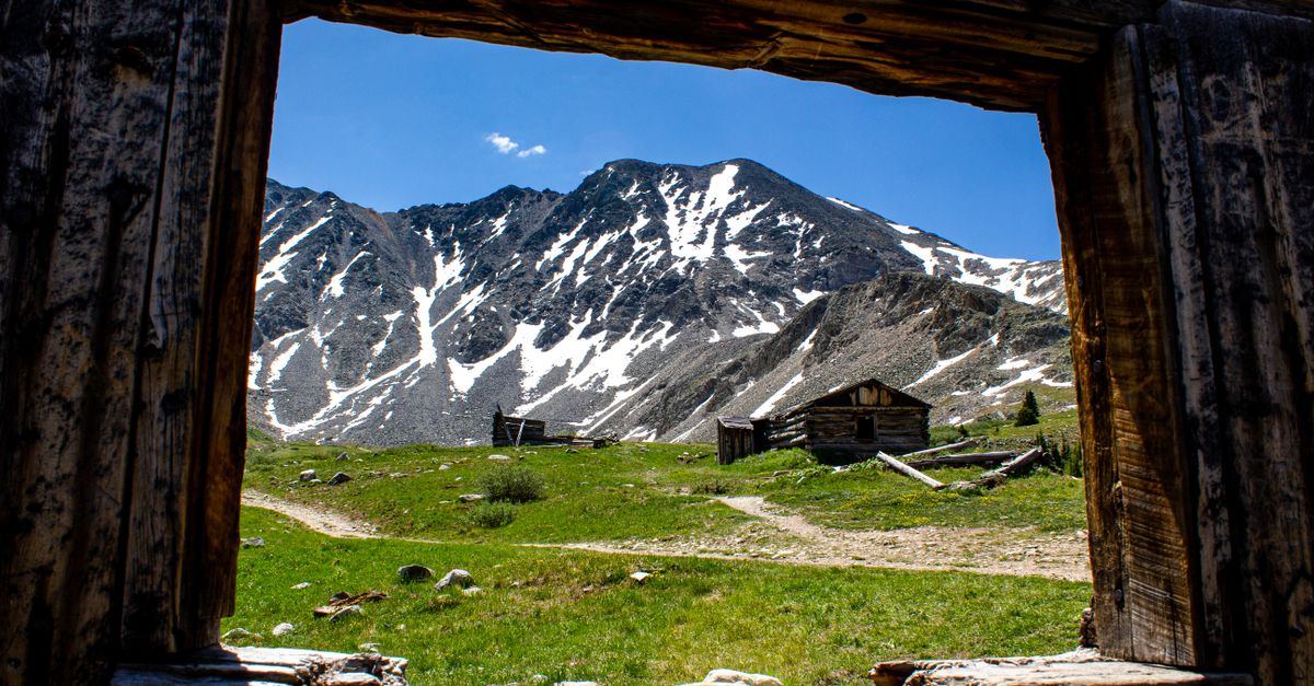 Capture of snow-capped mountains framed by an abandoned cabin in Frisco, Colorado.