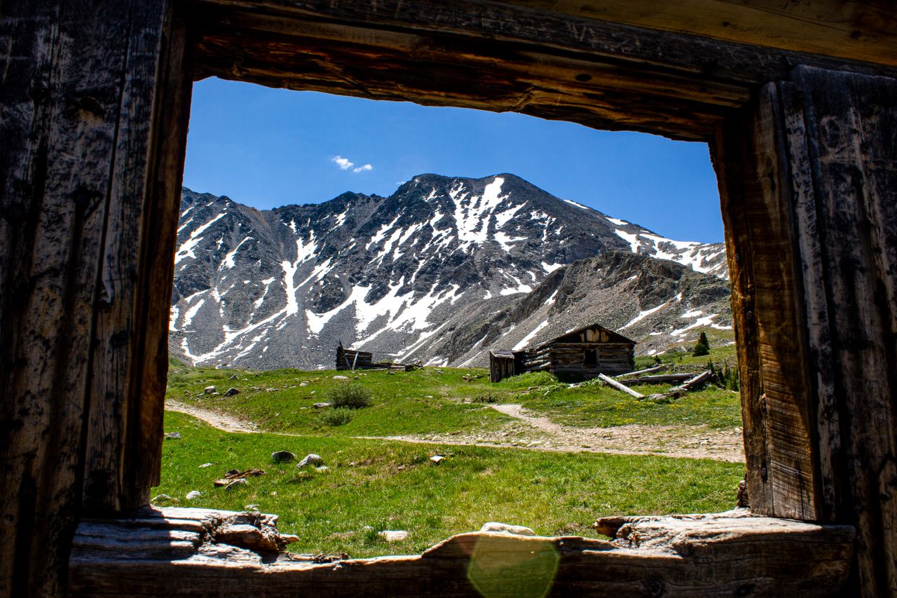 capture of snow capped mountains framed by an abandoned cabin in frisc