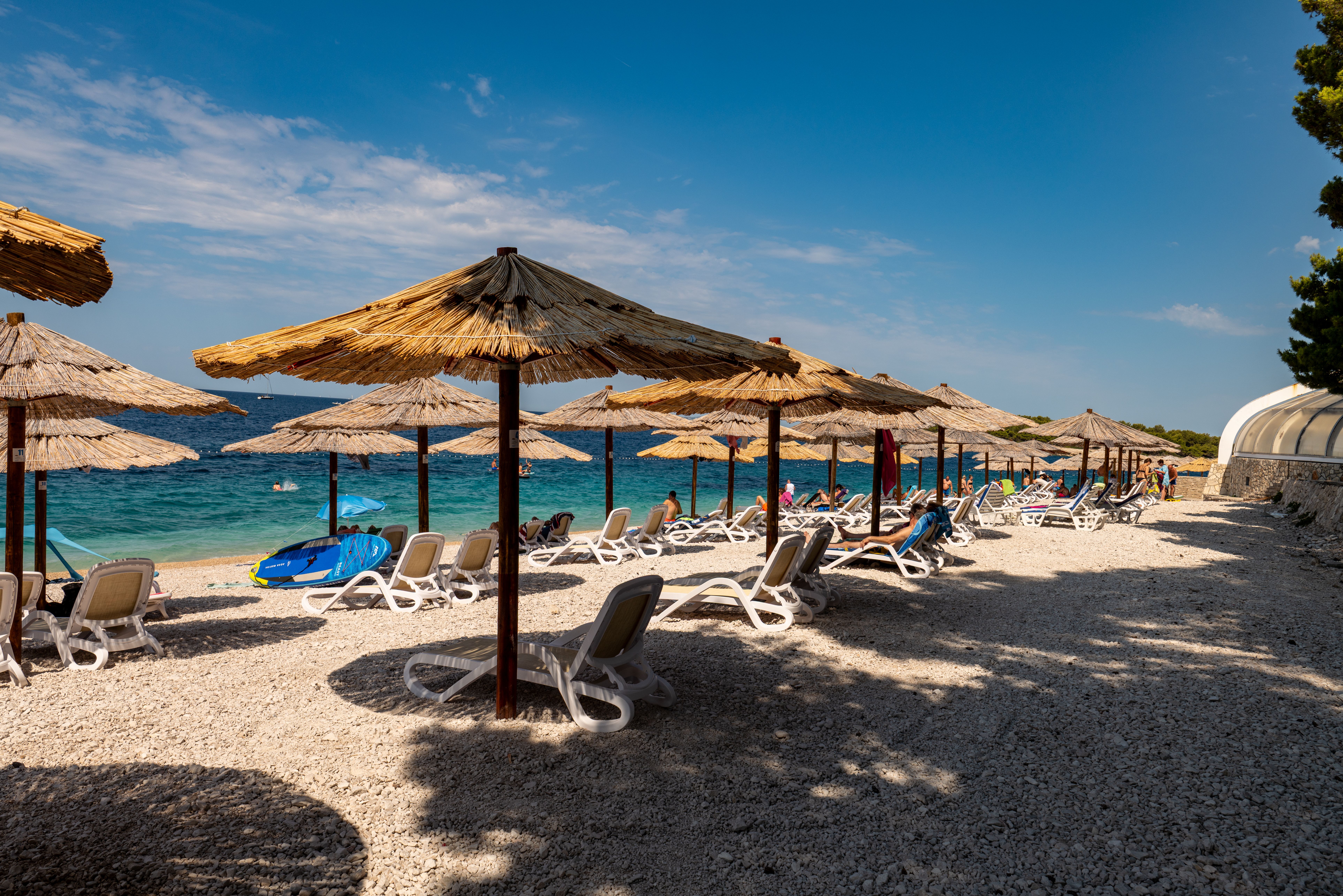 Serene day at Primošten beach with sun loungers and umbrellas under a clear sky.