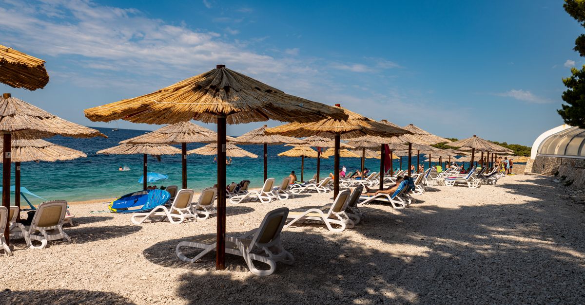 Serene day at Primošten beach with sun loungers and umbrellas under a clear sky.