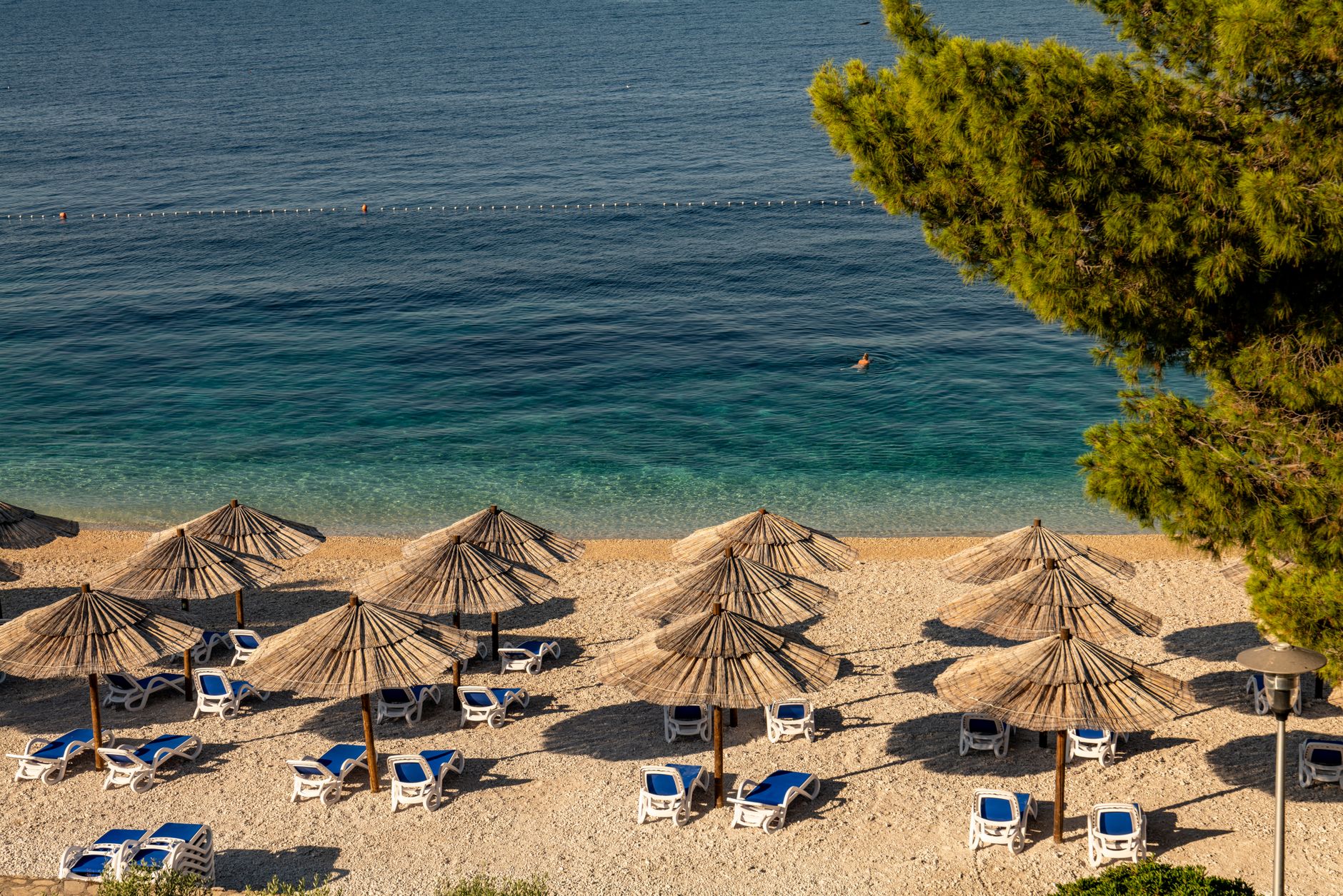 Relaxing beach scene in Primošten, Croatia with sun umbrellas, lounge chairs, and clear blue water.