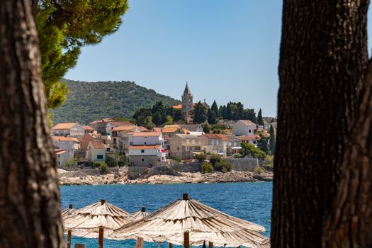 Charming Primošten with stunning Adriatic Sea view framed by trees and sunshades.