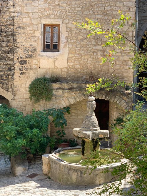 Free Rustic stone courtyard in a quaint French village with a central fountain and greenery. Stock Photo