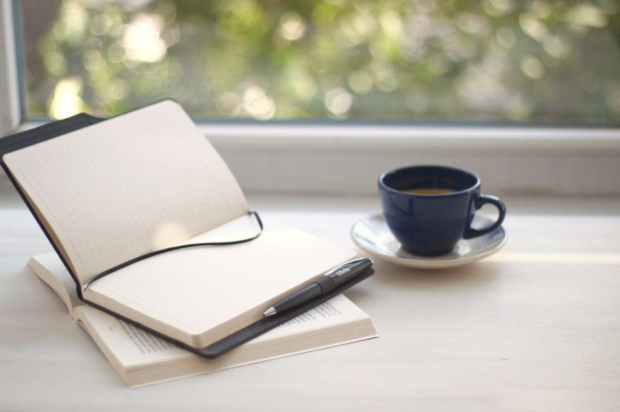 An open notebook and a cup of coffee on a sunlit windowsill