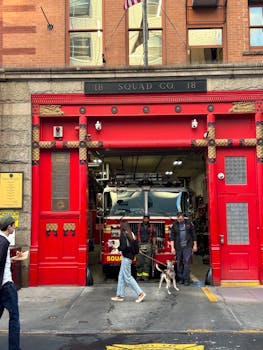Fire truck in iconic red fire station in Chelsea, NYC with people and dog nearby.