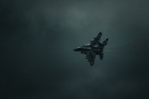 A military jet fighter flying through a dramatic dark sky, showcasing power and speed.