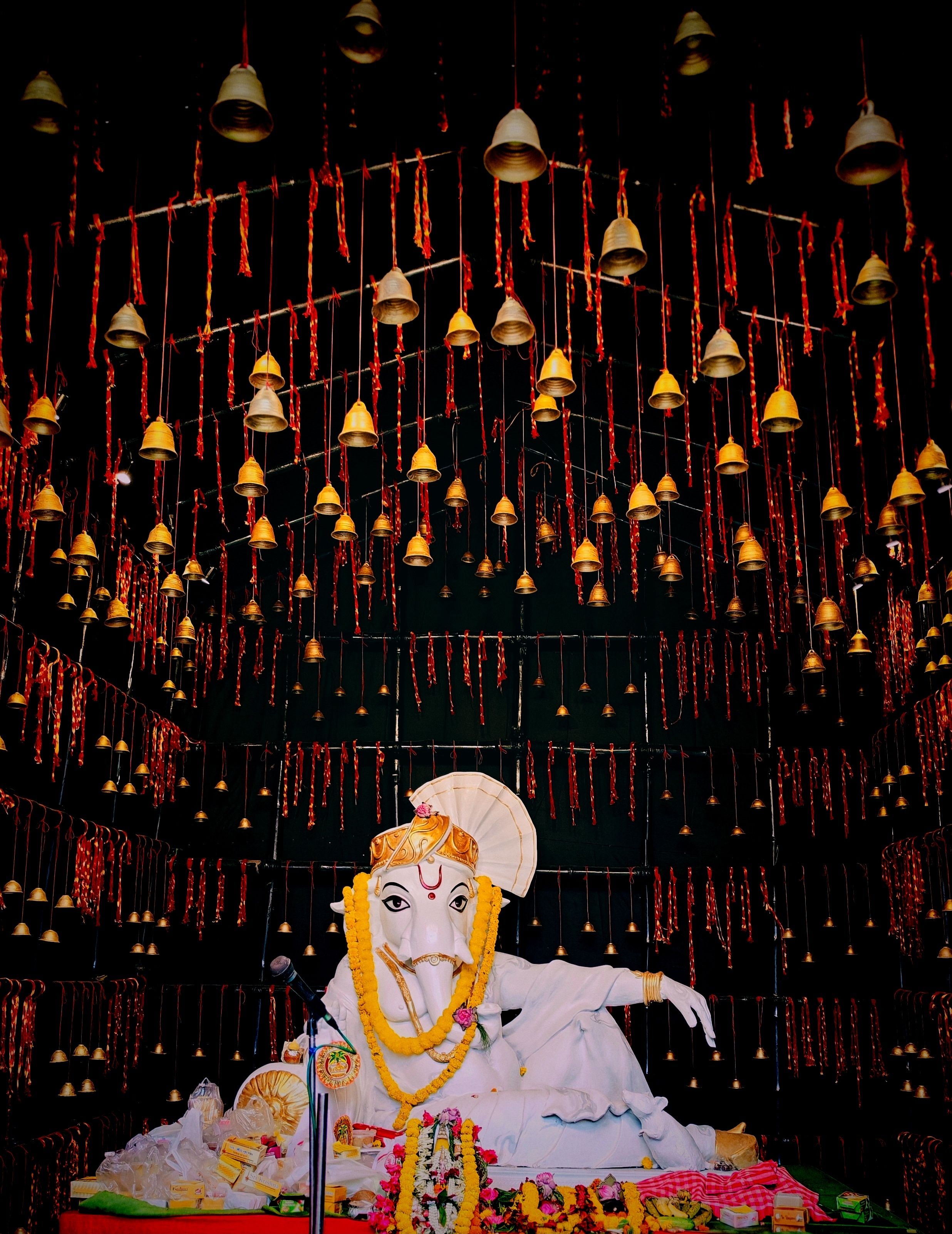 A detailed Ganesha statue adorned with marigold garlands and surrounded by hanging bells, exuding spiritual grace.