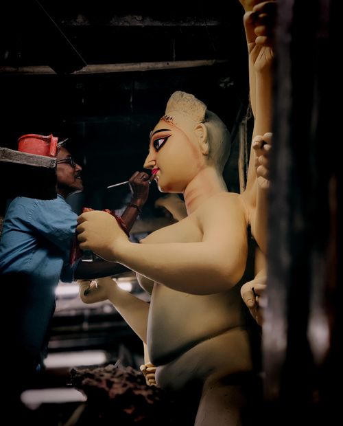 Free A skilled artisan carefully paints large traditional sculptures in a dimly lit workshop. Stock Photo